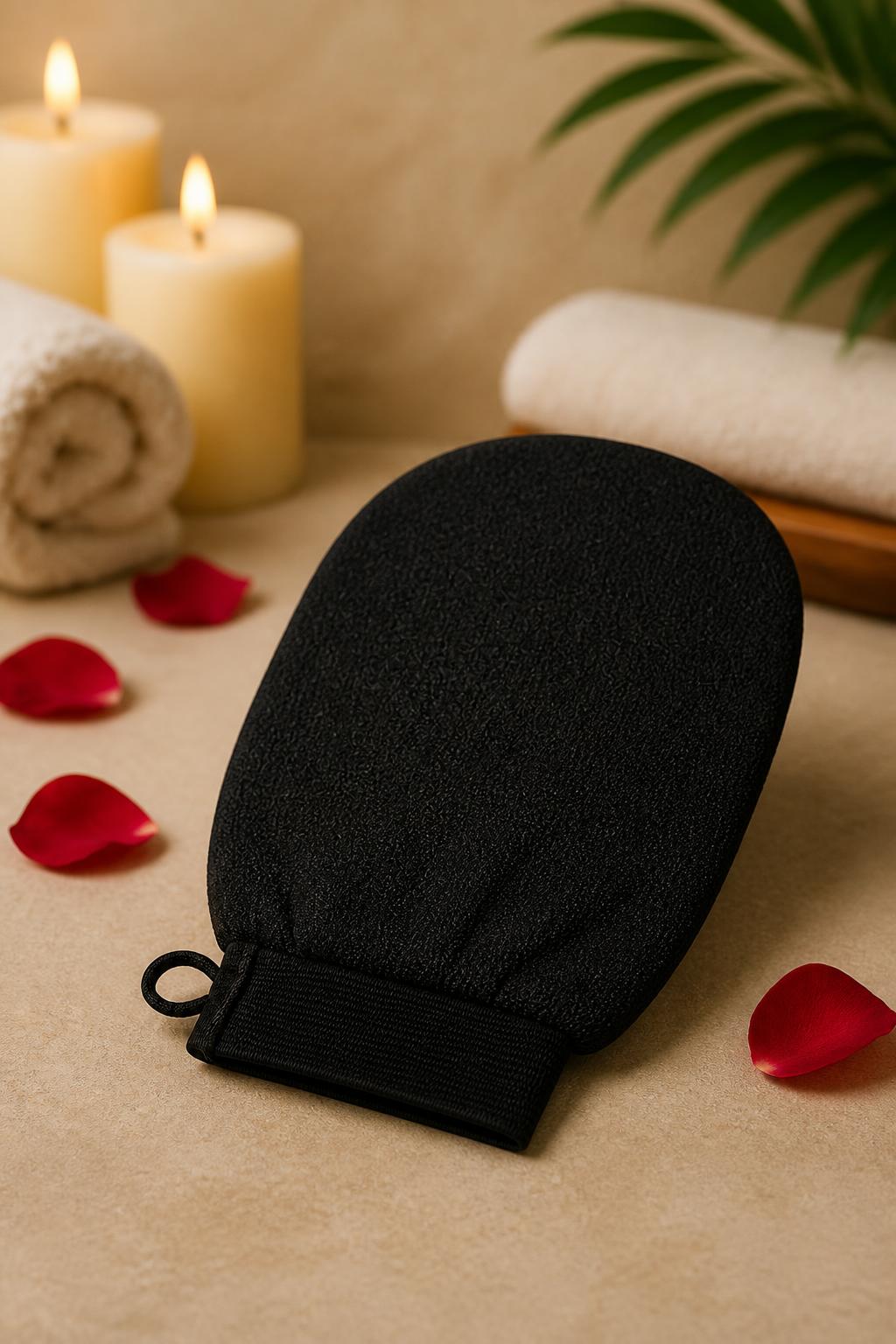 Black exfoliating loofah glove on a spa table with candles, towel and rose petals