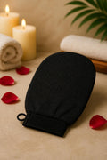 Black exfoliating loofah glove on a spa table with candles, towel and rose petals